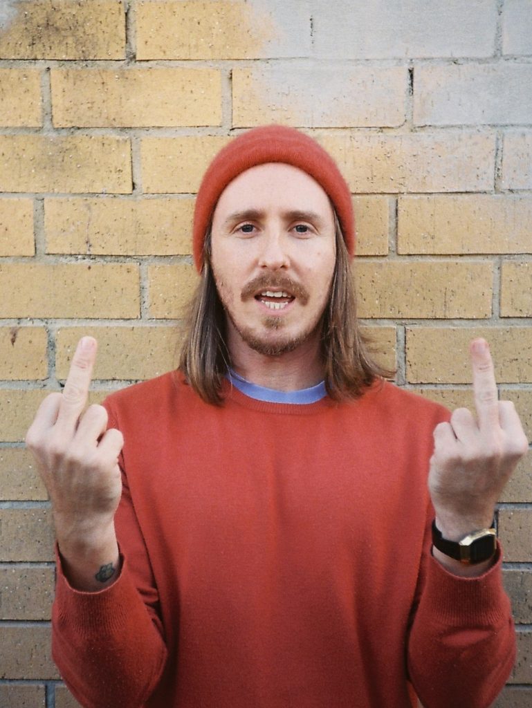 Jordan Lawrence wearing a maroon beanie and flipping the bird against a brick wall.