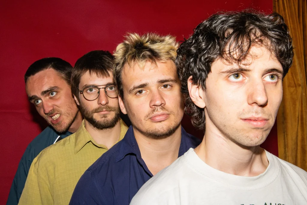 Radium Dolls band members in a close-up portrait against a red backdrop