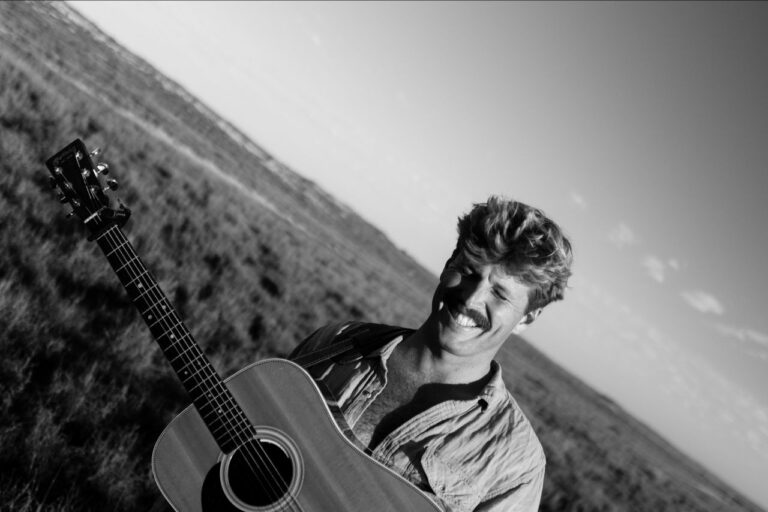 Ziggy Alberts smiling outdoors with an acoustic guitar